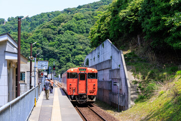 山陰本線餘部駅で電車を待つ乗客と入線するオレンジ色の電車