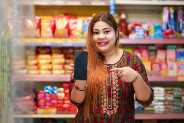 Indian woman showing smartphone screen at grocery shop.