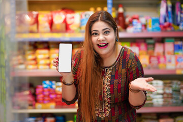 Indian woman showing smartphone screen at grocery shop.