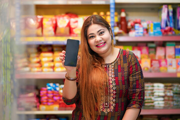 Indian woman showing smartphone screen at grocery shop.