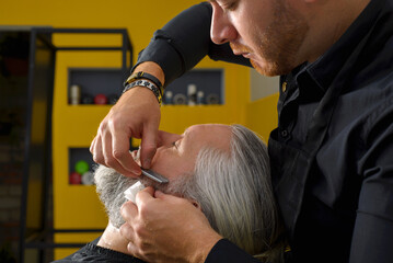 Barber cutting and styling the beard of a gray-haired man. Beard cutting and styling process. Barber shop for men.