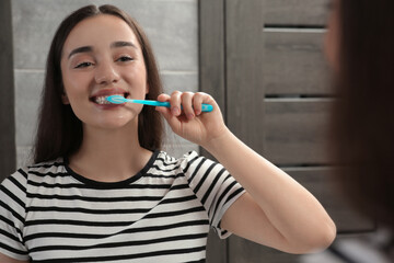 Young woman brushing her teeth with plastic toothbrush near mirror in bathroom