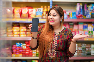 Indian woman showing smartphone screen at grocery shop.