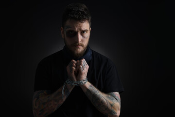 Man with bruise chained on dark background. Hostage