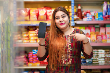 Indian woman showing smartphone screen at grocery shop.