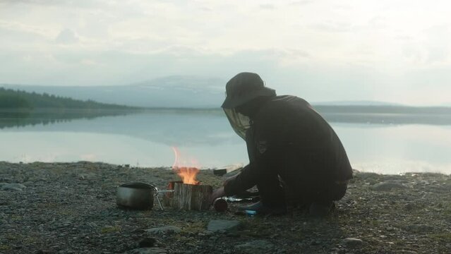 Hiker Cooking on a Camping Stove with a Mosquito Hat, Beautiful Lake and Sunset Atmosphere on the Kungsleden Trail in Northern Sweden, Adolfström