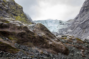 Hike to Franz Josef glacier, Waiau, seen from glacial valley below, blue ice and mountain, rocks, grey cloudy sky, alps, South Island, New Zealand, NZ