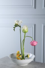 Stylish ikebana as house decor. Beautiful fresh flowers on grey table near white wall