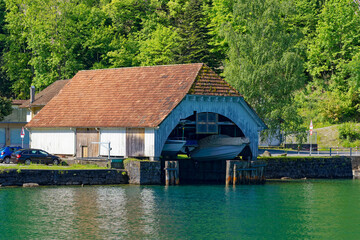 Fototapeta na wymiar Scenic view boat house with Lake Lucerne in the foreground on a sunny spring day. Photo taken May 22nd, Isleten, Canton Uri, Switzerland.