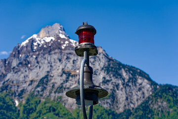 Fototapeta na wymiar Mountain panorama at Swiss village of Flüelen with red light at pier in the foreground on a sunny spring morning. Photo taken May 22nd, 2023, Flüelen, Canton Uri, Switzerland.