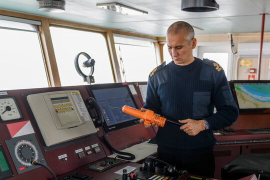 Officer on watch with SART on the navigational bridge. Caucasian man in blue uniform sweater using search and rescue radar transponder on the bridge of cargo ship.