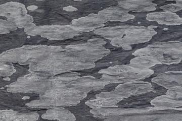 Black glossy background with irregular light gray spots. Winter, frost. Paper, texture. Design space.