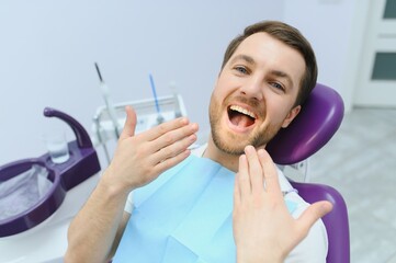 Handsome man smiling while teeth exam. Happy male patient sitting in a dentist's chair and having...