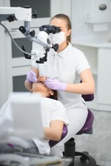 Female dentist using dental microscope treating patient teeth at dental clinic office