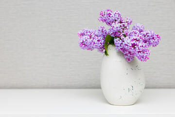 a vase with a lilac flower is on the table.