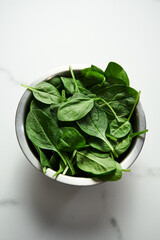 A bunch of Fresh baby spinach leaves in the in a stainless steel bowl on white marble background.