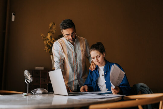 Boyfriend standing near non-binary person sorting bills on table at home