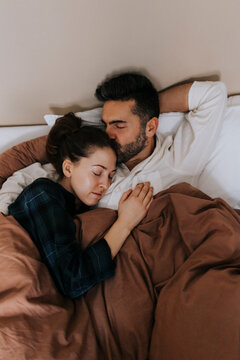 High angle view of man kissing non-binary person relaxing in bed at home