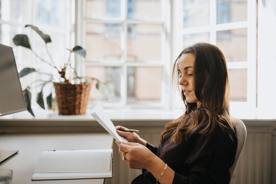 Side view of businesswoman examining document sitting at office