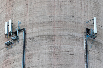 A close-up of the mobile phone antennas installed on wall of a tall power plant chimney. Object against the blue sky on a sunny day.