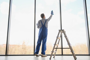 Young man cleaning window in office