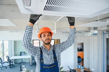 Concentrated young Indian engineer setting up air conditioner.