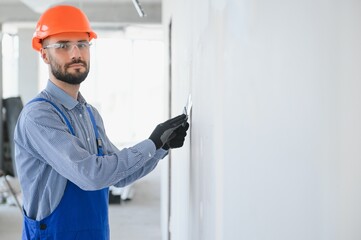 man drywall worker or plasterer sanding and smoothing a plasterboard walls with stucco using a sandpaper holder. Wearing white hardhat and safety glasses. Panoramic image with copy space