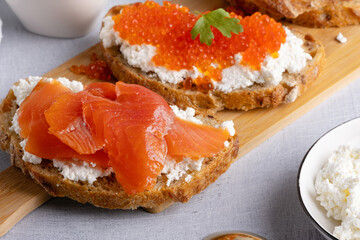 Sandwiches with red caviar, cottage cheese and salted salmon. Wooden cutting Board. Close up