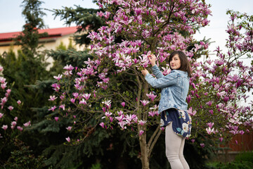 Tender woman in jeans jacket enjoying nice spring day near magnolia blooming tree. Springtime activities.