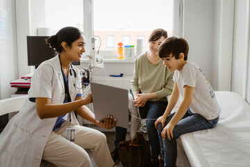 Female pediatrician showing tablet PC to mother and son sitting in examination room at clinic