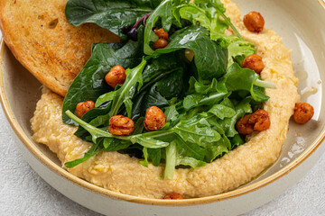 Portion of gourmet hummus with greens and toasts