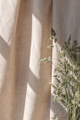 Sunlight shadows on beige linen curtain, meadow grass bouquet, aesthetic summer boho background with sun ray