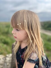 little blonde girl with flowers in her hair stands against the sky. Soft focus. 