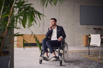 A melancholic businessman in a wheelchair sitting with a sad expression, gazing through the window of a modern office, conveying a sense of solitude