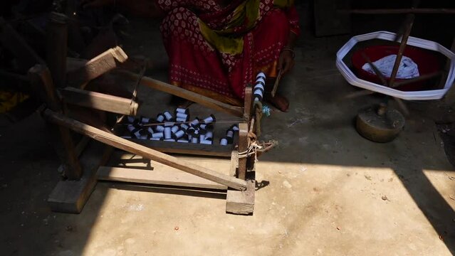 Woman spinning cotton thread by hand outside her house. The yarn is twisted into a reel through a process to make cloth. 