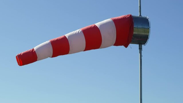 Windsock is waving in the wind against a clear blue sky. Close-up view of the airport wind gauge indicates wind direction and strength. 4k footage