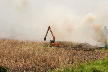 heavy earth mover vehicle accumulating dry straw stubble for burning on the agricultural field with smoke coming out from stubble burning