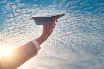 a hand holds a  toy paper plane against the sky, freedom and flights, ticket discounts
