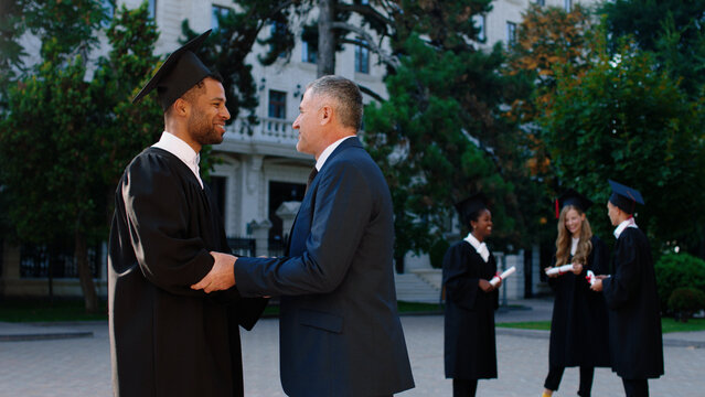 In the college garden graduation day college professor old man congrats his student and giving diploma to him multiracial concept. ARRI Alexa Mini.