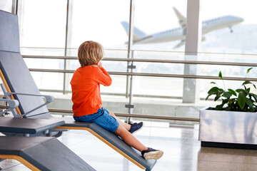Young boy eagerly watches planes from airport chair