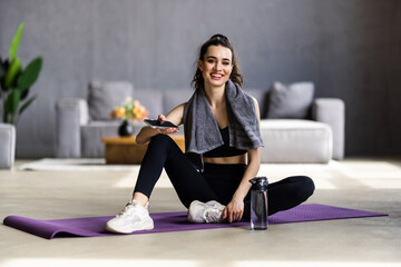 Satisfied fitness blogger resting after workout at home with water, woman take break on mat at...