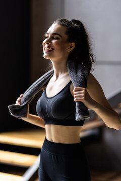 Smiling sporty woman in sportswear having break after exercising at home carrying towel on her shoulders