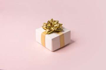 Fototapeta premium One white gift box with golden ribbon on pink background still life.