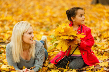 Young mother playing with her daughter in autumn park