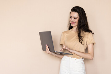 Naklejka premium Portrait of gorgeous woman standing and holding laptop over beige background
