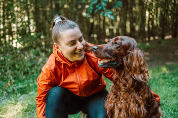 Happy caucasian woman hiker hiker walks with her cute Irish Setter dog on a walk in a summer...