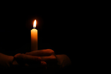 Woman holding burning candle in hands on black background, closeup. Space for text