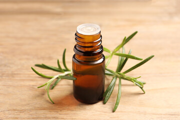Bottle with essential oil and fresh rosemary on wooden table