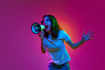 Portrait of serious young woman, girl shouting via loudspeaker over pink background in neon light....