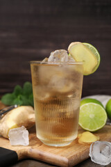 Glass of tasty ginger ale with ice cubes and ingredients on wooden table